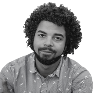 Man with curly hair and beard wearing a patterned button-up shirt against a white background.